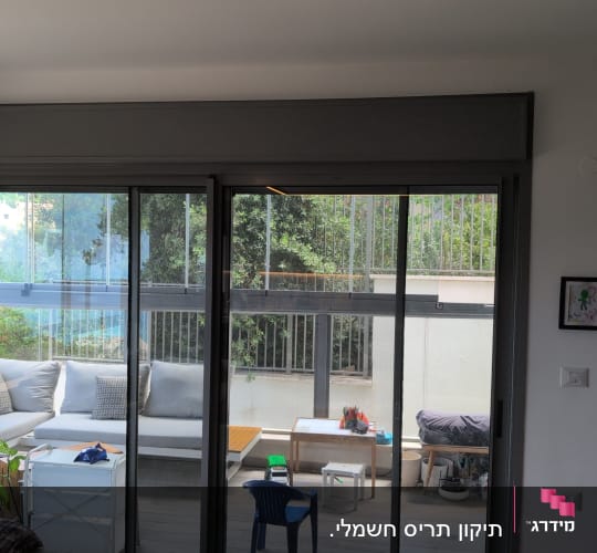 תריסים על חלון זכוכית בסלון עם נוף לחצר